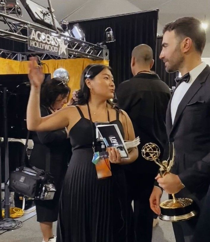 Jenna Frank Asian woman in black gown. At red carpet event with celebrity from Apple TV holding a Emmy